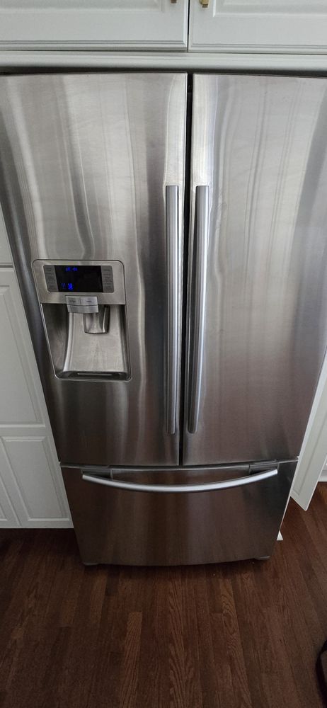 A stainless steel refrigerator is sitting on a wooden floor in a kitchen.