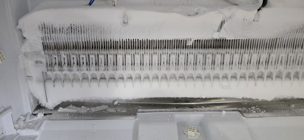 The inside of a refrigerator is covered in snow and ice.