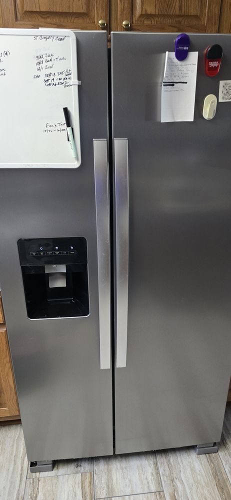 A stainless steel refrigerator with a dry erase board on top of it.