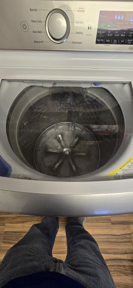 A person is standing next to a washing machine with the lid open.