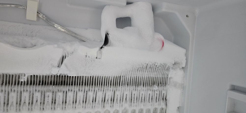 The inside of a refrigerator is covered in snow and ice.