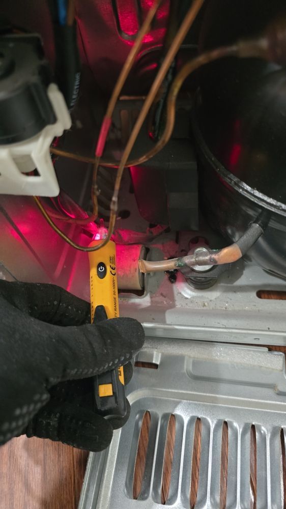 A person is holding a screwdriver in front of a refrigerator.