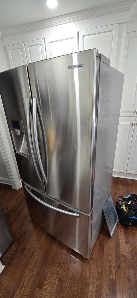 A stainless steel refrigerator is sitting on a wooden floor in a kitchen.