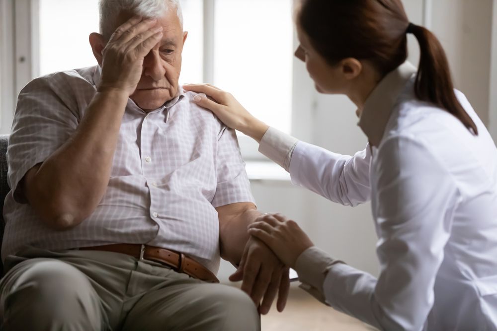 Older man with his head in his hand, being consoled by a younger woman with a hand on his shoulder.