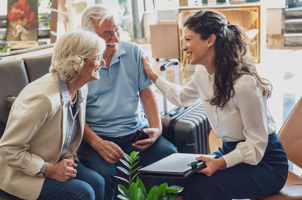 Woman assisting a senior couple with travel plans, smiling, and touching the man's shoulder.