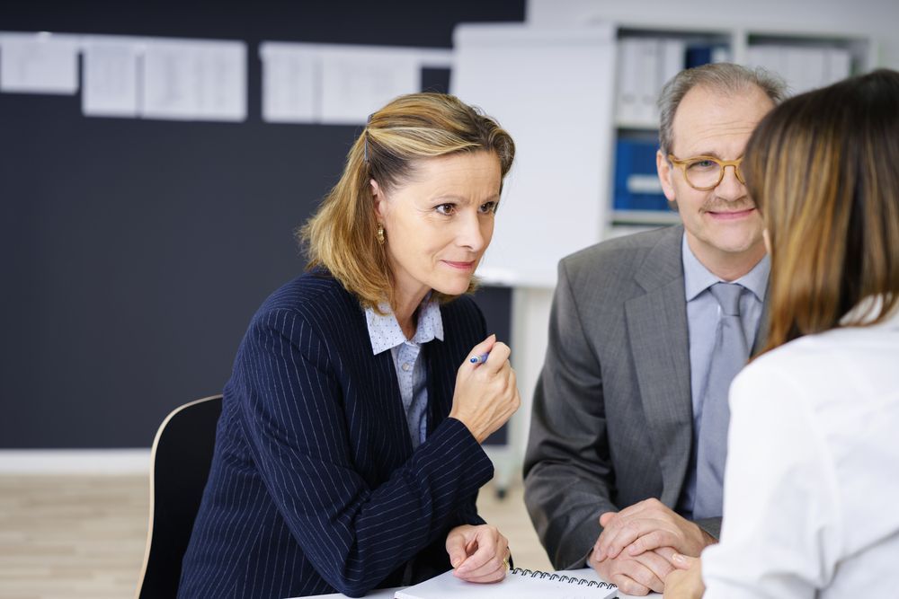 Three people in a meeting: woman speaking, man smiling, another woman's back to camera.
