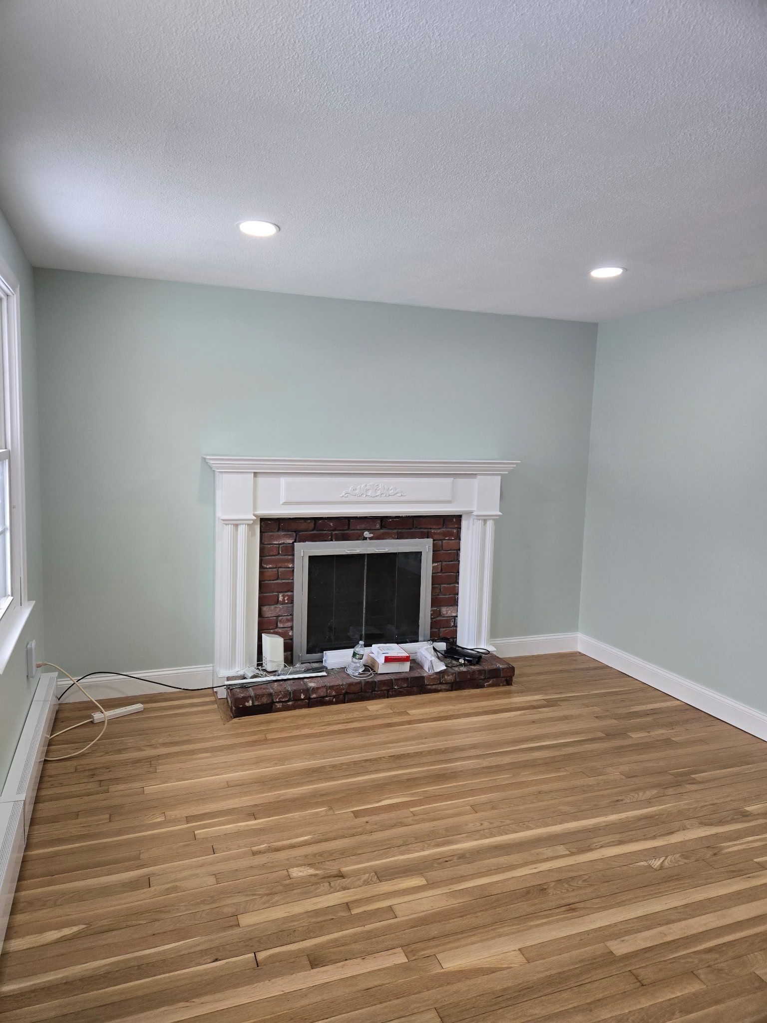 Empty living room with mint walls, white fireplace mantel, and hardwood floor under recessed lights