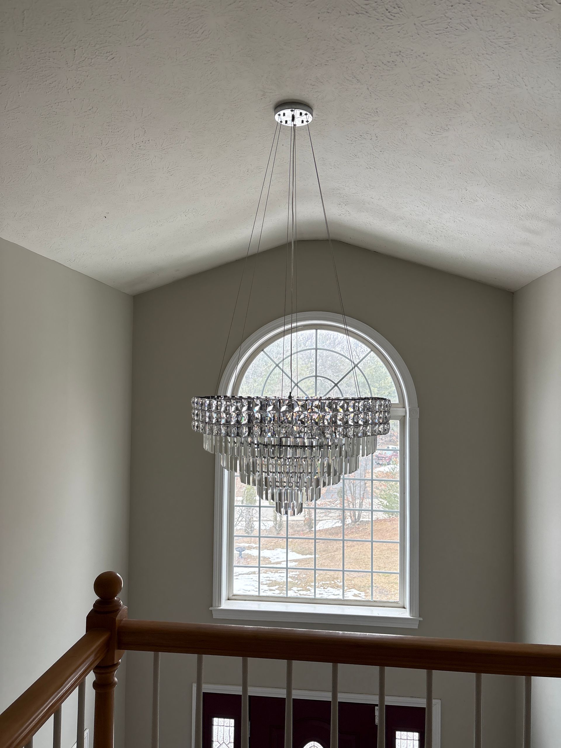 Crystal chandelier hanging in a staircase foyer beneath a large arched window