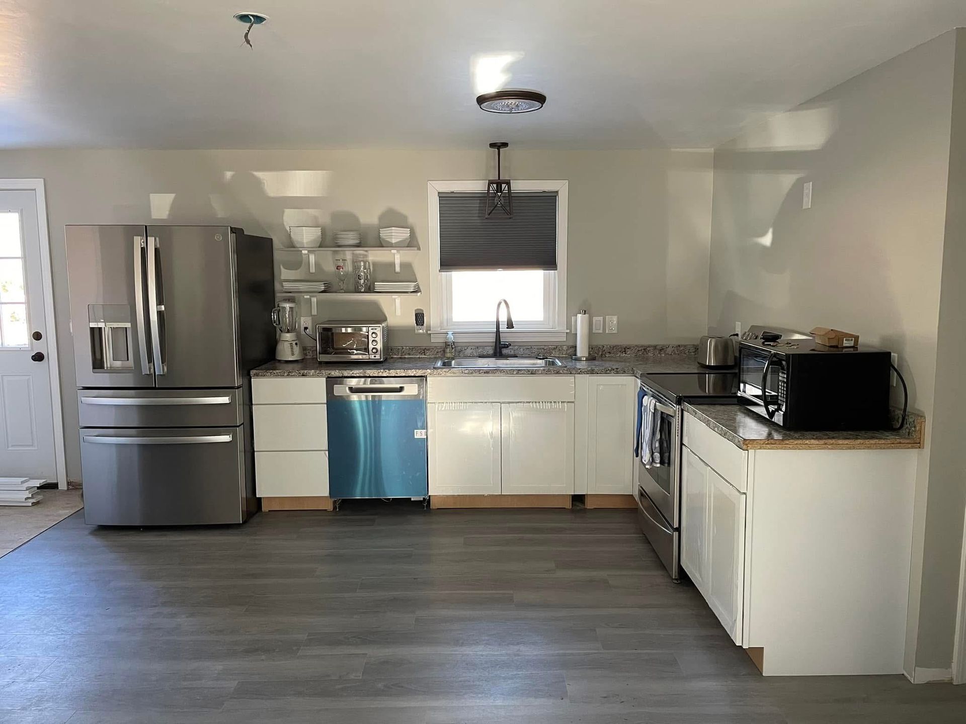 Kitchen with stainless steel appliances, white cabinets, and gray flooring.