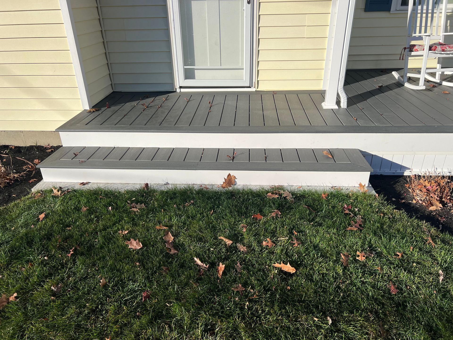House porch with gray decking, white steps, and grass in front