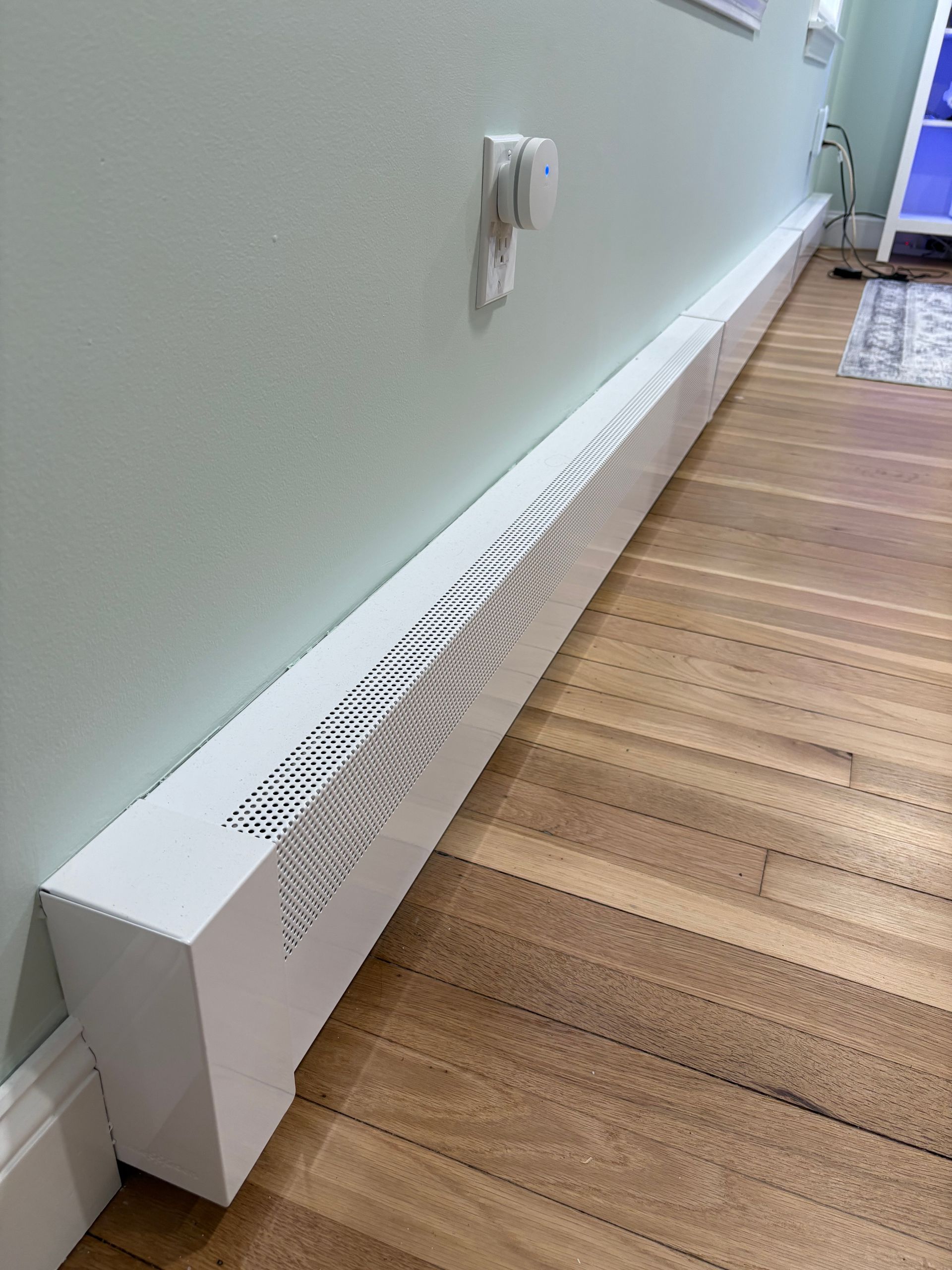 White baseboard heater along a light green wall beside a hardwood floor in a hallway