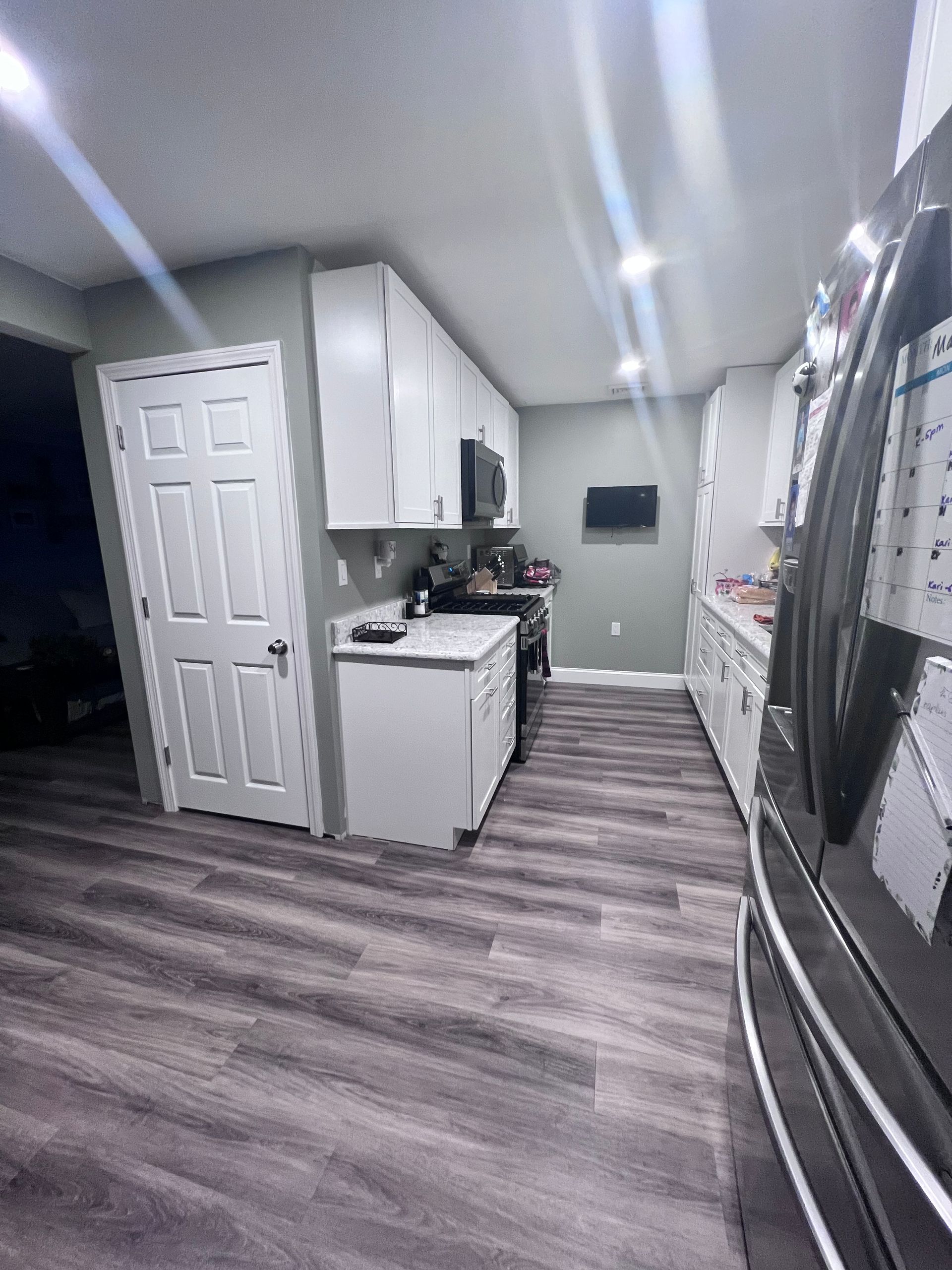 Bright kitchen with white cabinets, gray flooring, and stainless-steel refrigerator under recessed lights