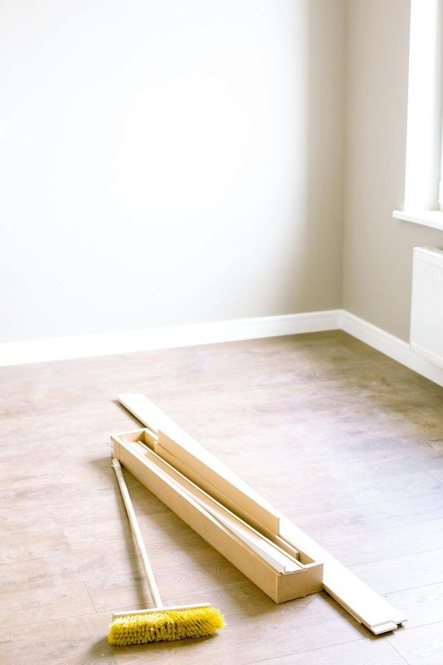 Empty room with wood flooring, beige walls, and window. A broom and molding sit on the floor.