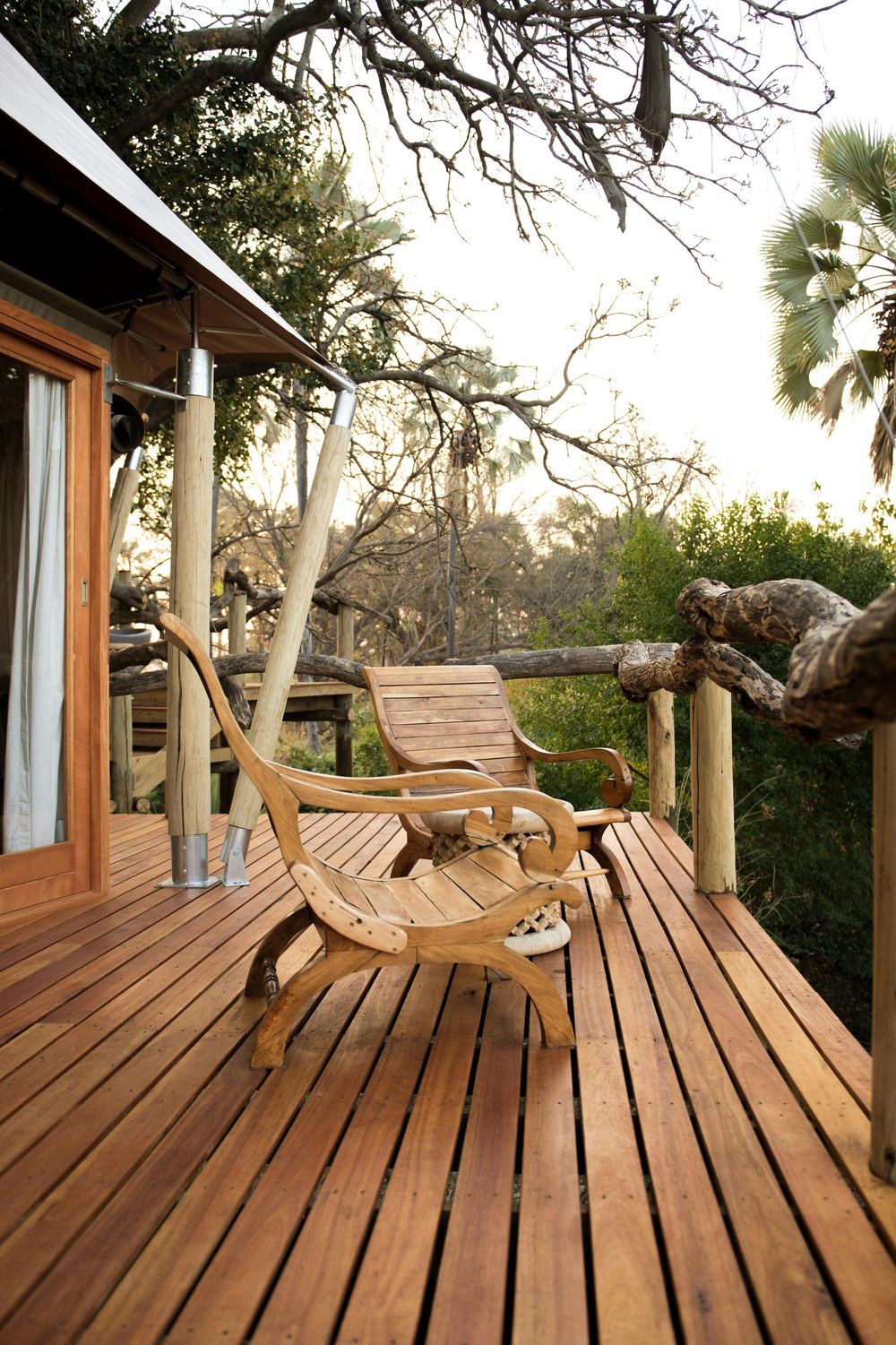 Wooden deck with two chairs, overlooking a tree-filled landscape. Bright sunlight.