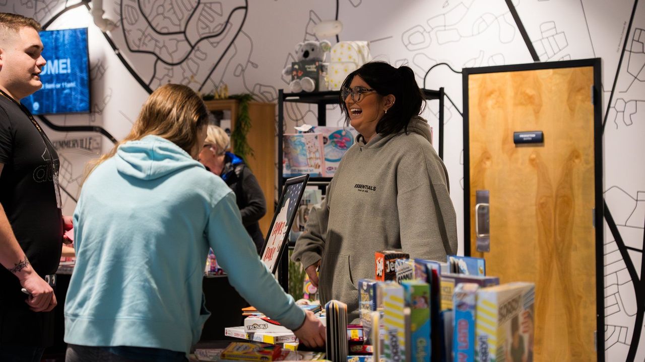 Voluntarios riendo juntos en una mesa con juegos y libros donados