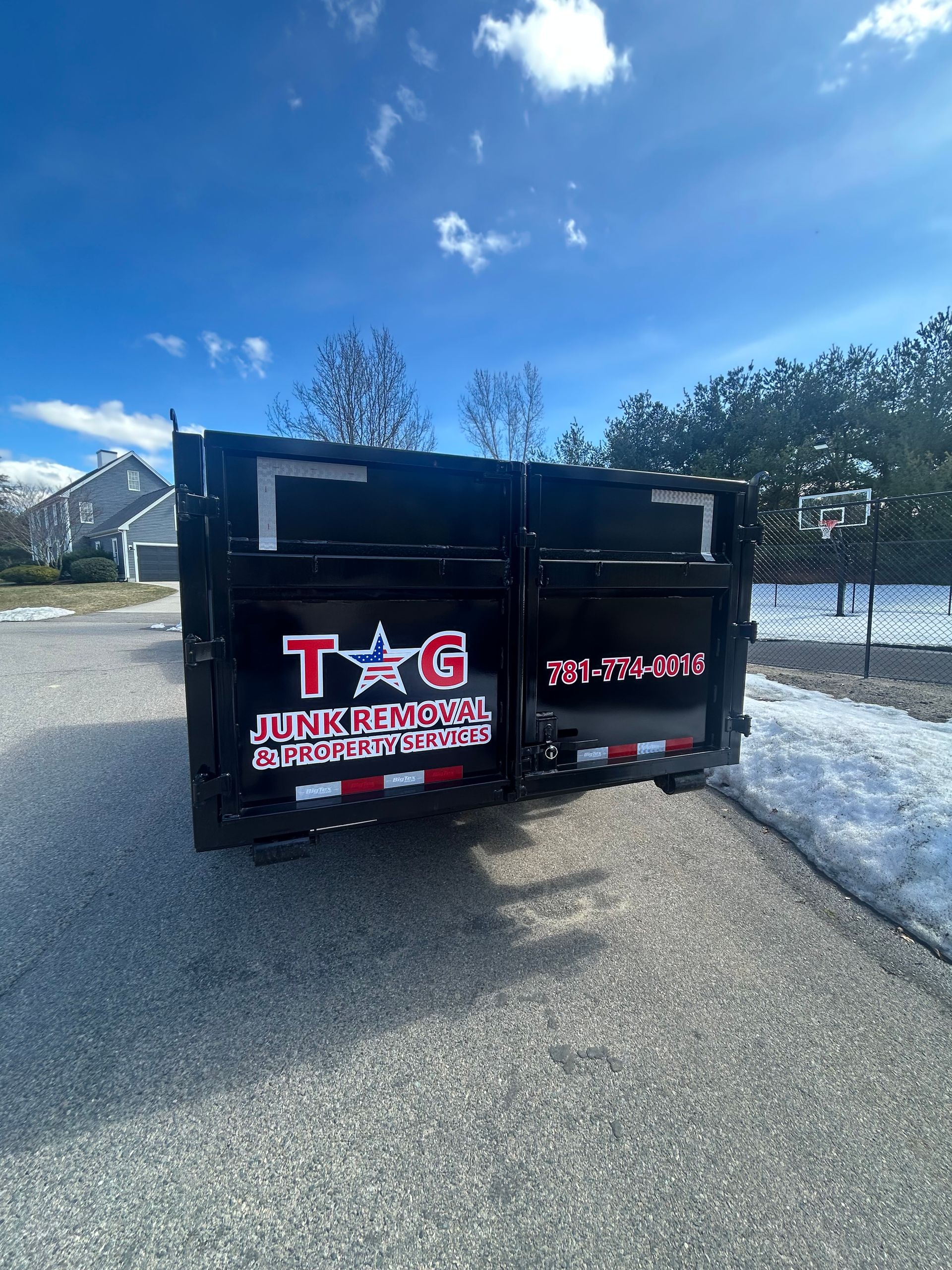 A black junk removal dump trailer parked on a snowy road with