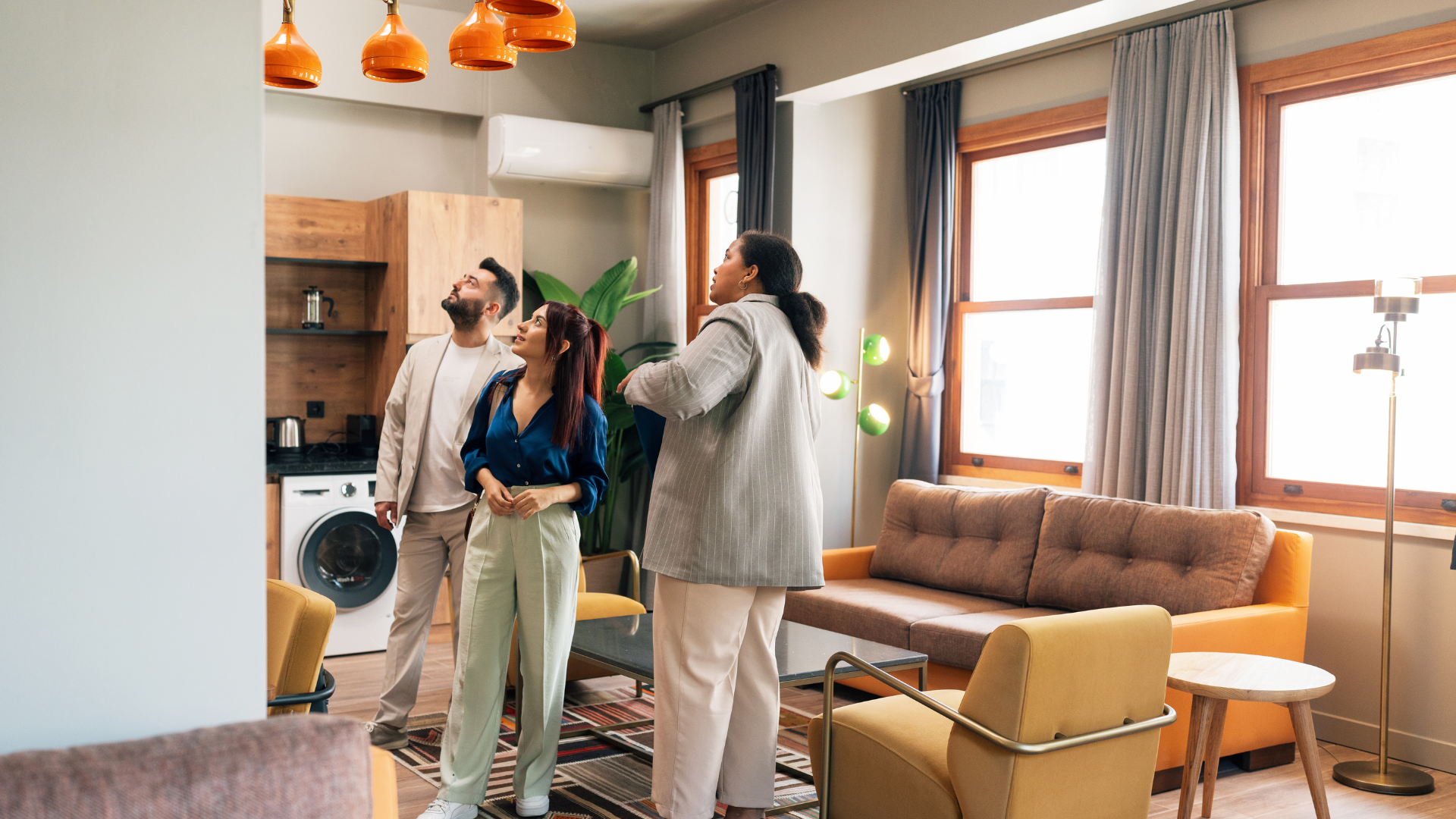 Three people looking up in a room with orange lights, a sofa, and large windows.