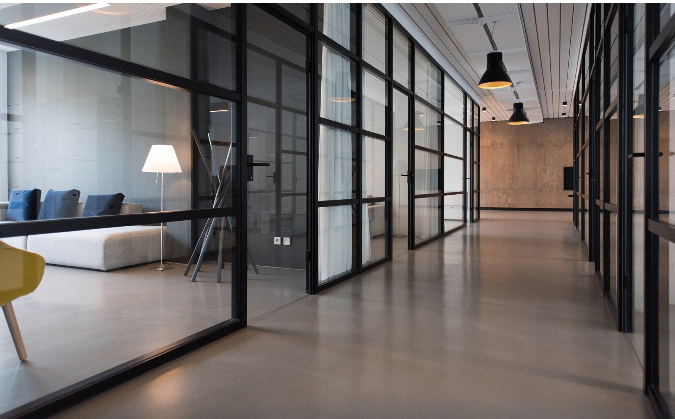 A long hallway in an office building with glass walls and chairs.