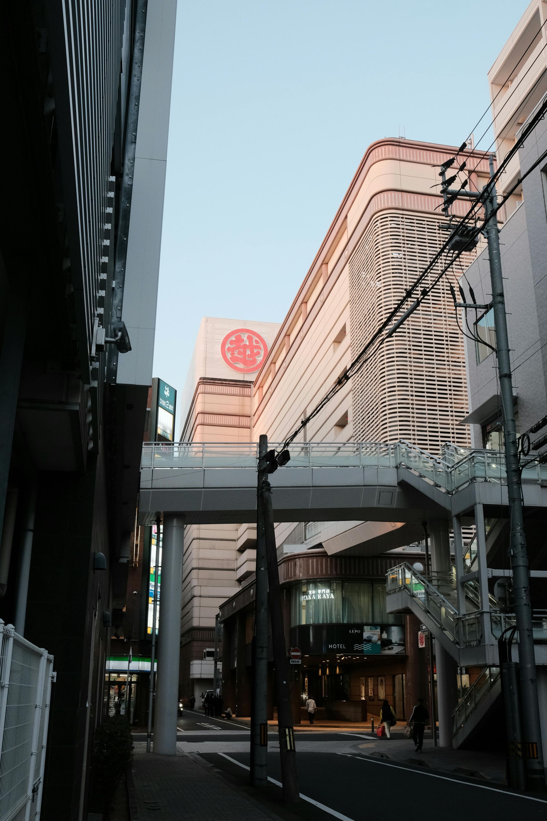 Street scene in Japan with pedestrian bridge and tall buildings. Pink and white buildings, blue sky.
