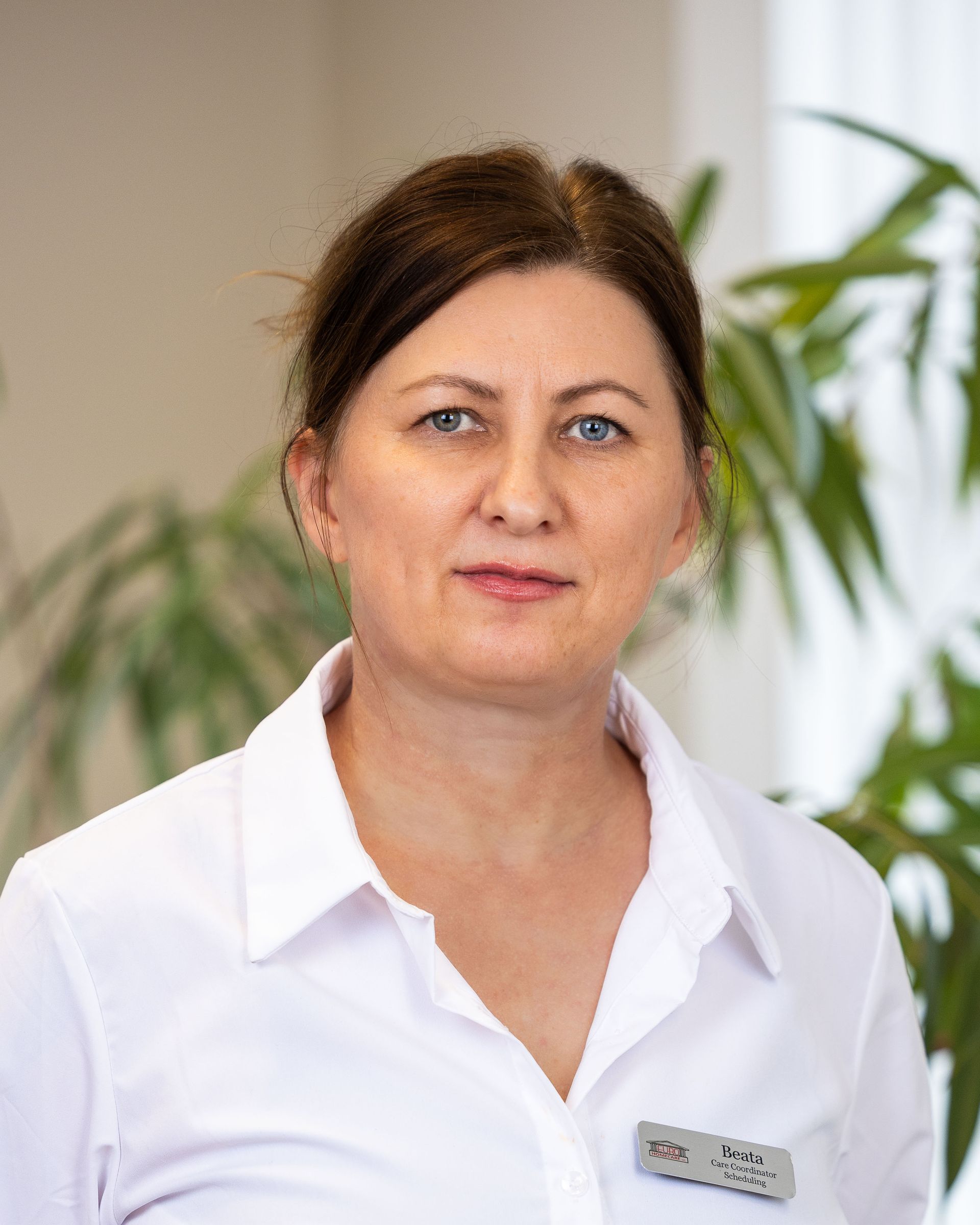 A woman in a white shirt is standing in front of a plant.