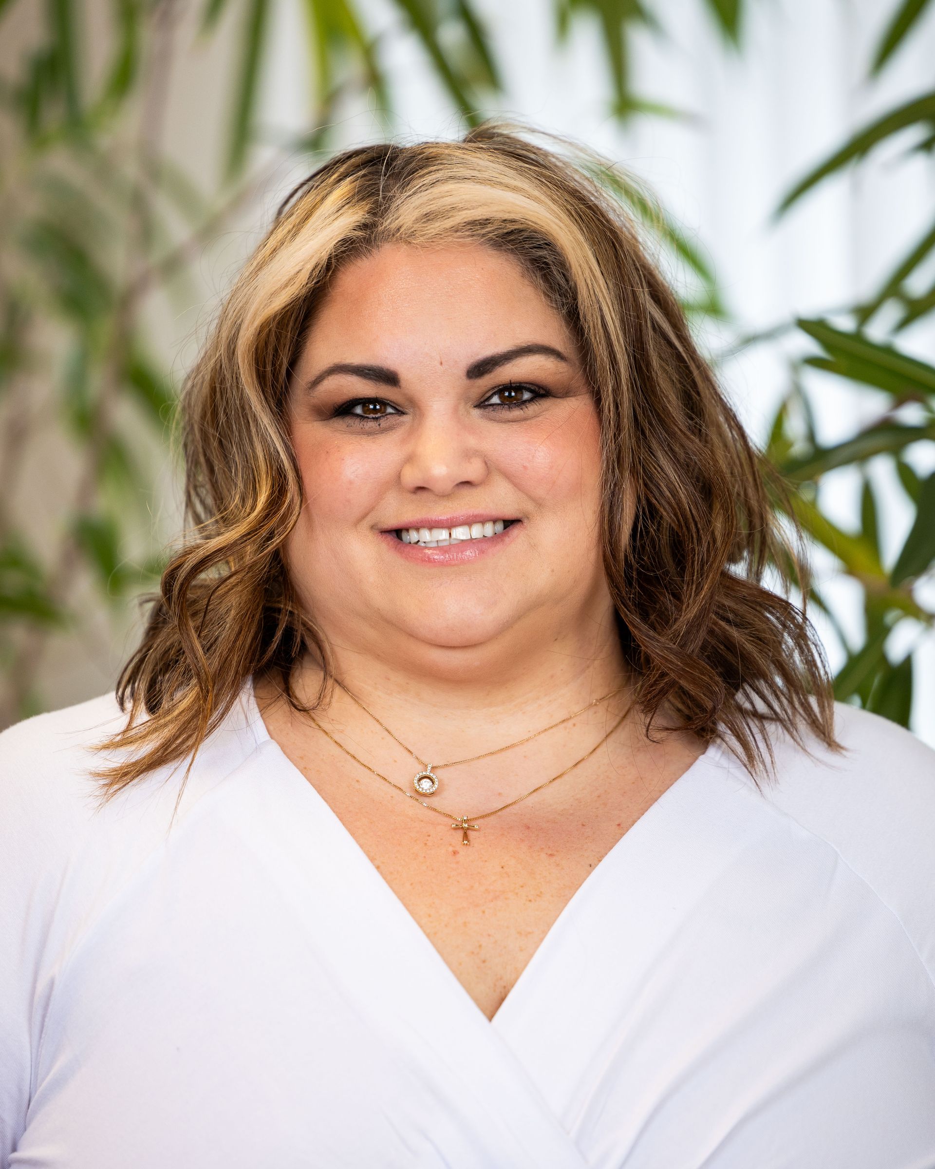 A woman wearing a white shirt and a necklace is smiling for the camera.