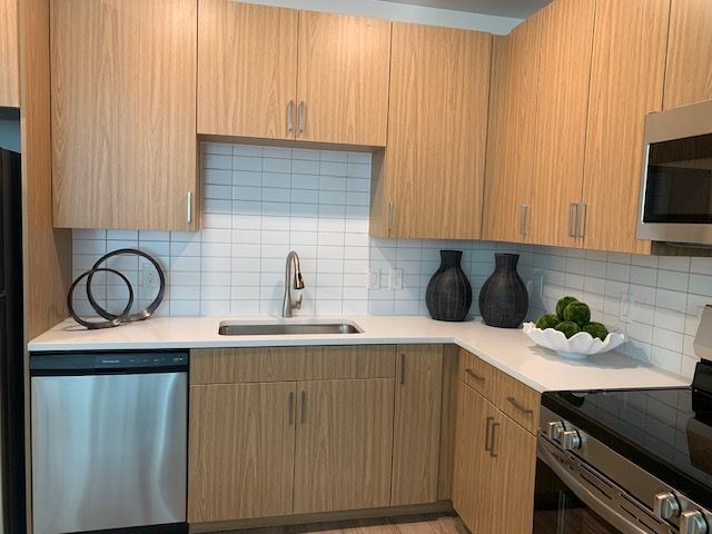 Modern kitchen with light wood cabinets, stainless appliances, white tile backsplash, and decorative vases.