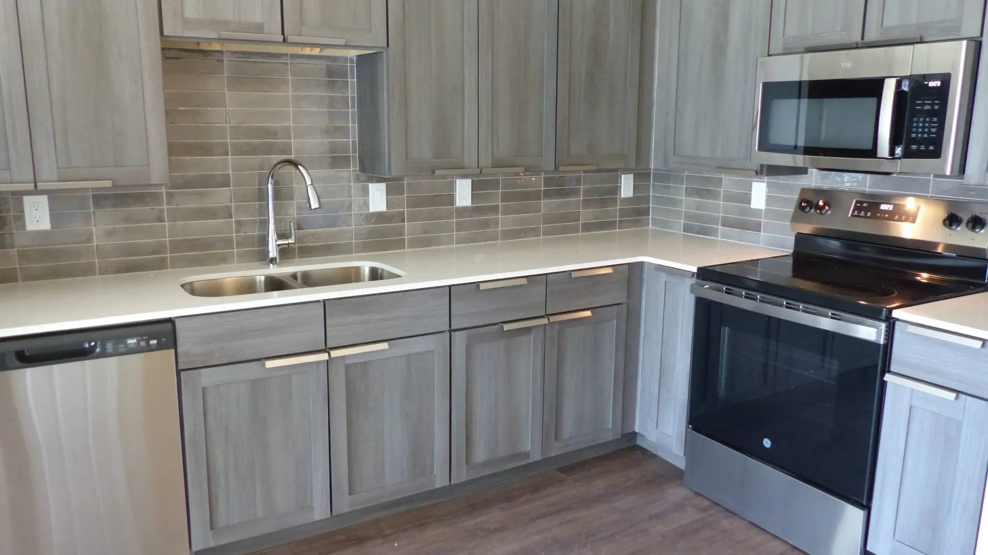 Modern kitchen with gray cabinets, stainless steel appliances, and stone backsplash