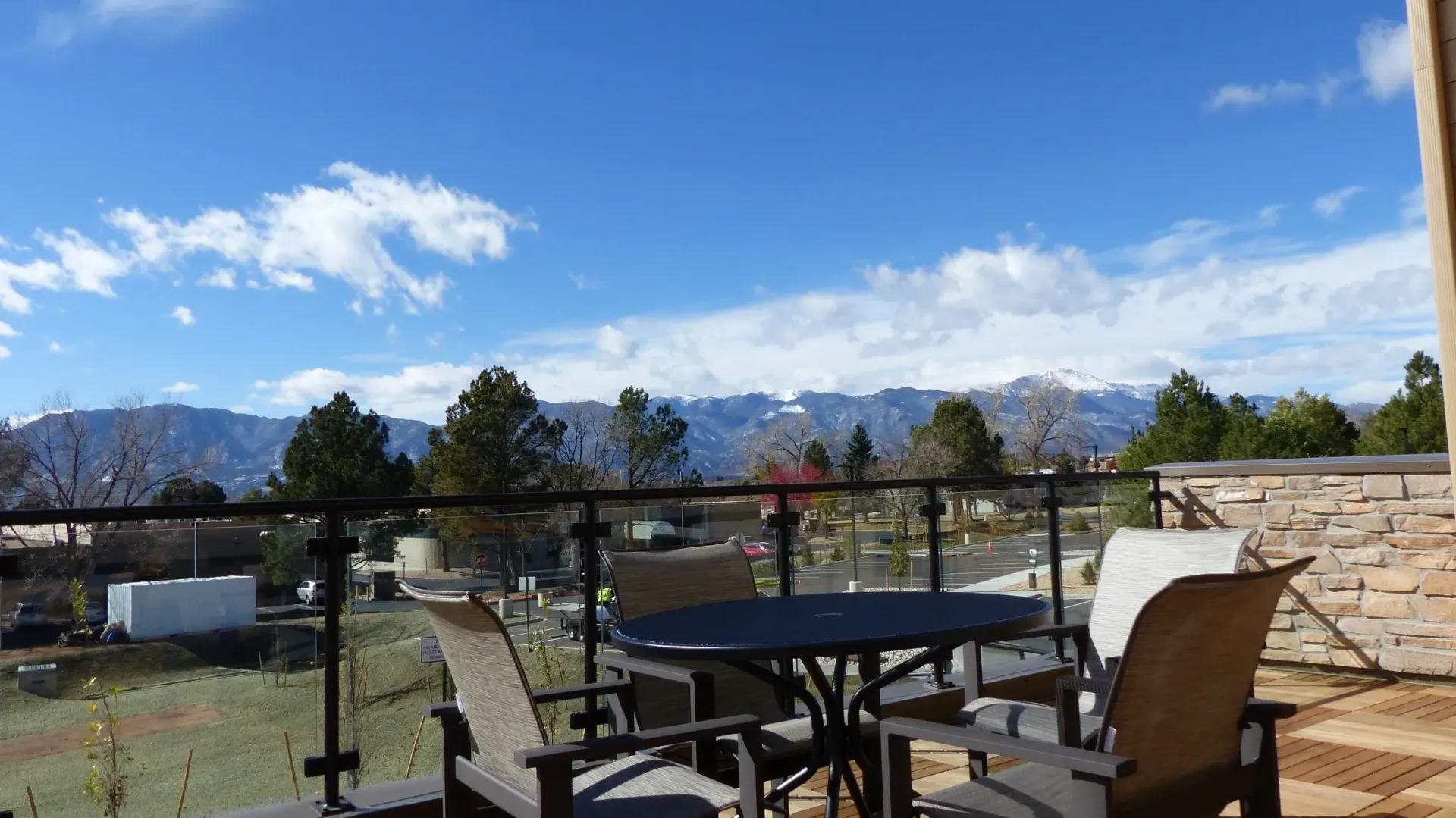 Patio table and chairs overlooking a grassy yard, mountains, and a blue sky with clouds
