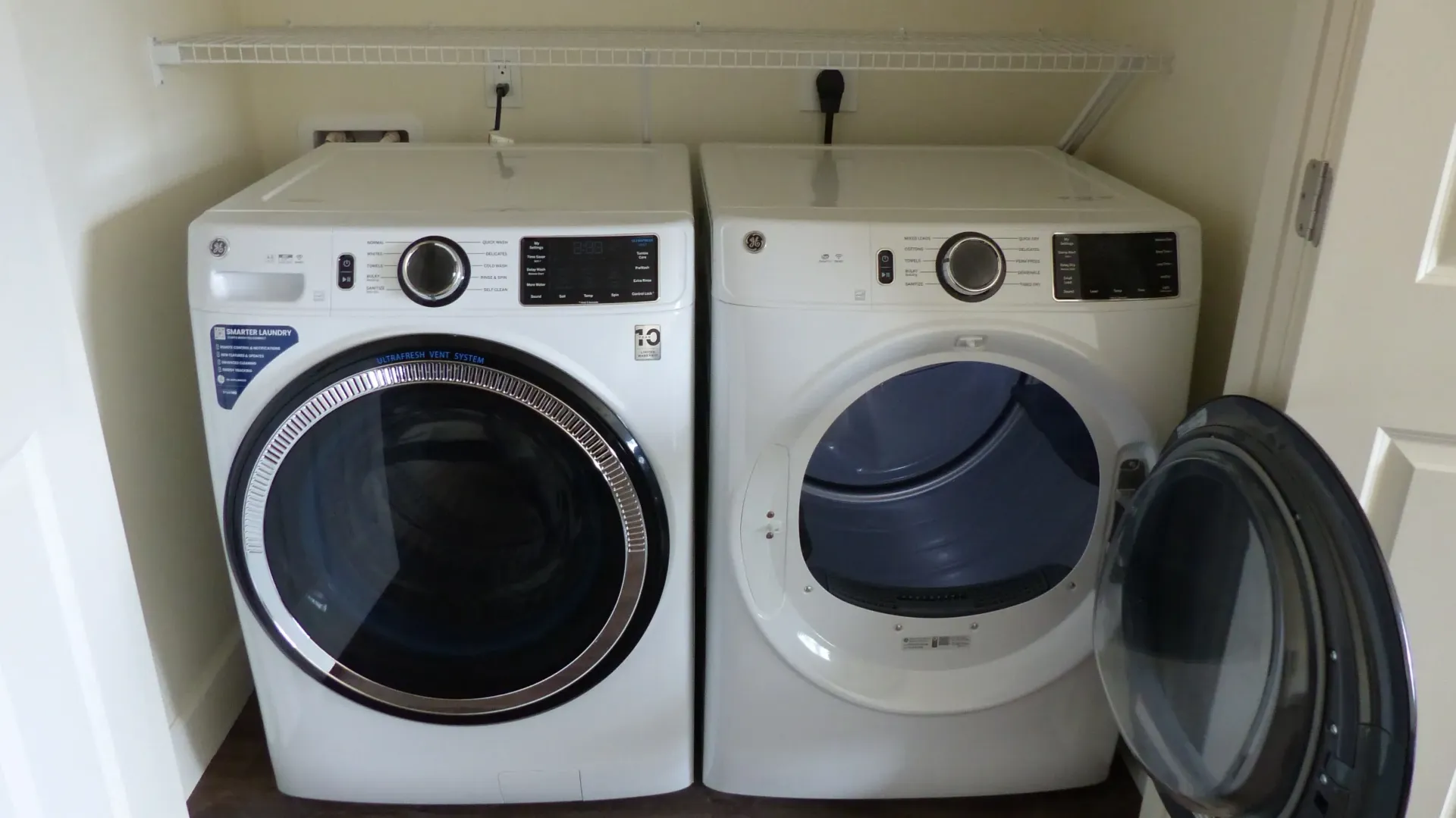 Two front-loading laundry machines in a closet, one door open on the right.