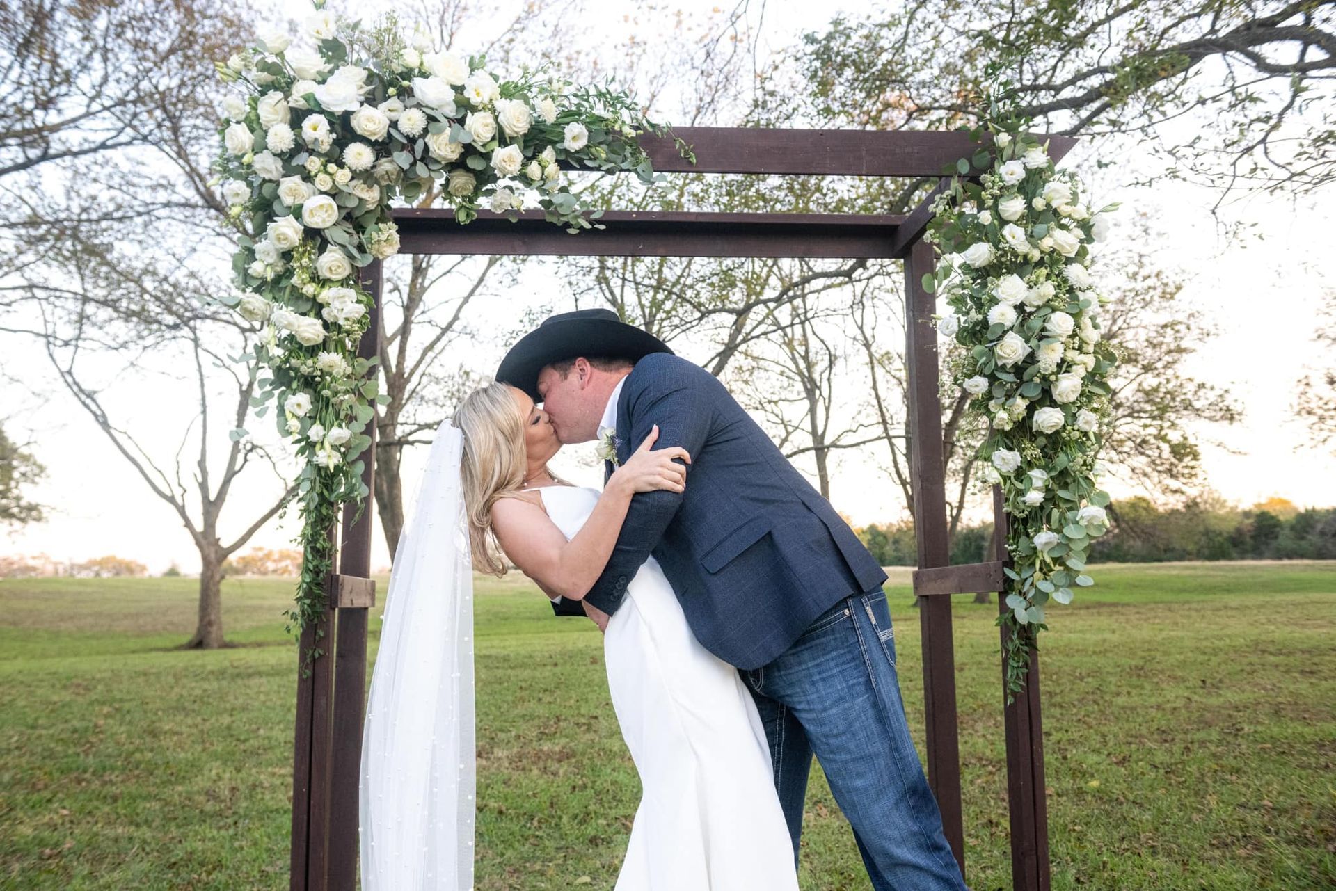 bride and groom kissing under wooden outdoor altar