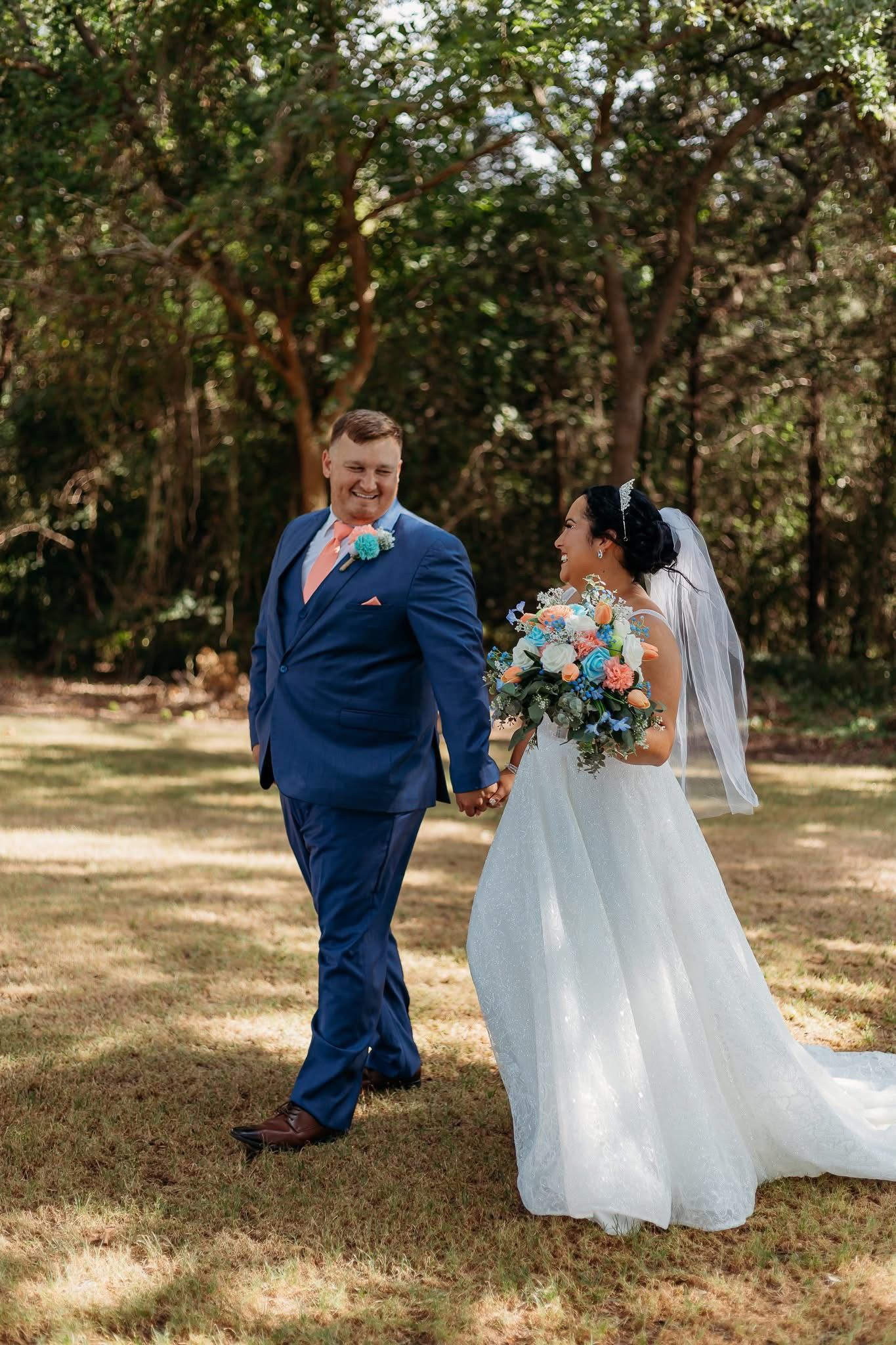 groom and bride smiling at each other surrounded by green trees