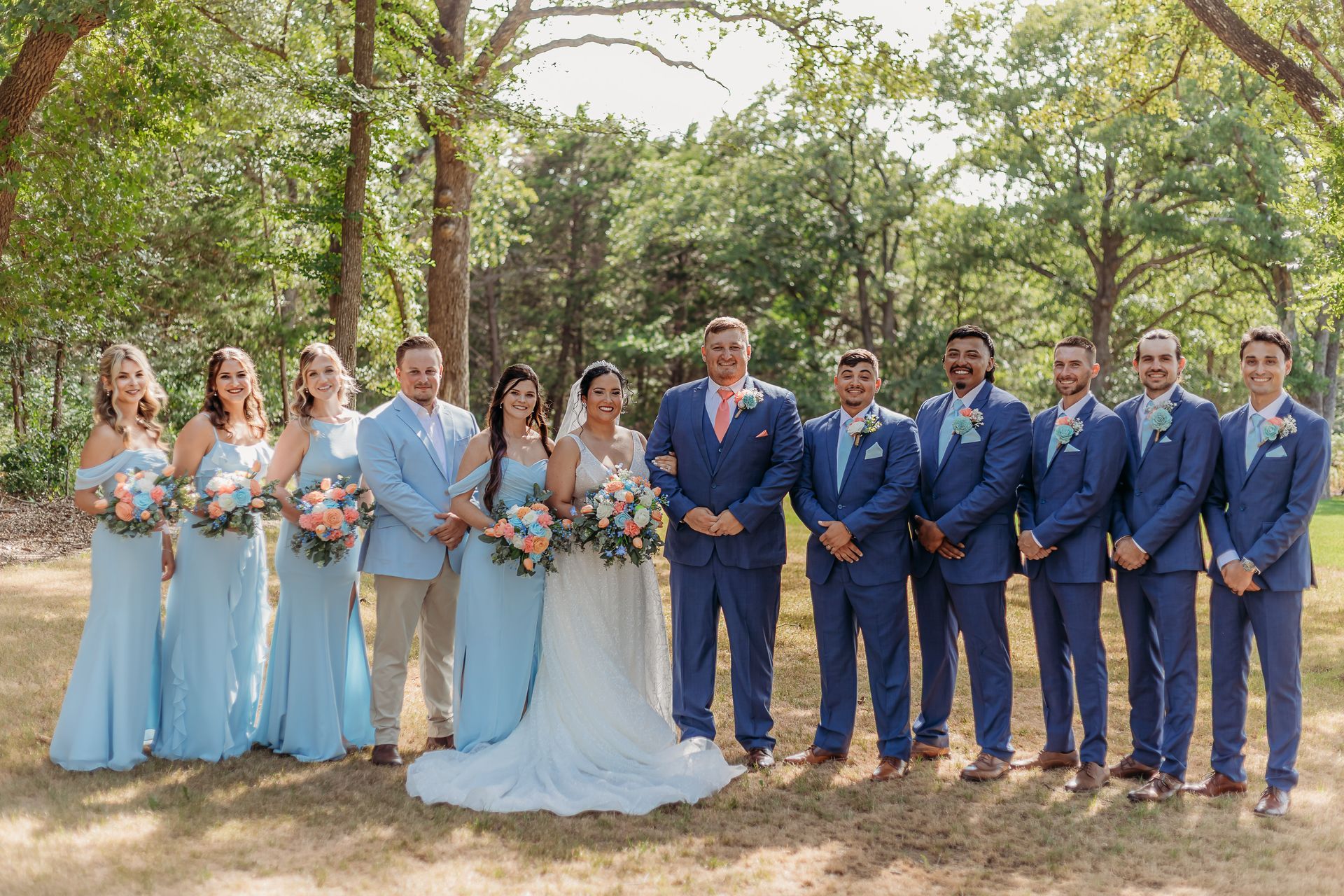bride and groom with wedding party surrounded by green trees