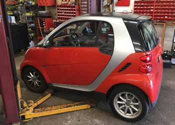 a red smart car is sitting on a lift in a garage .