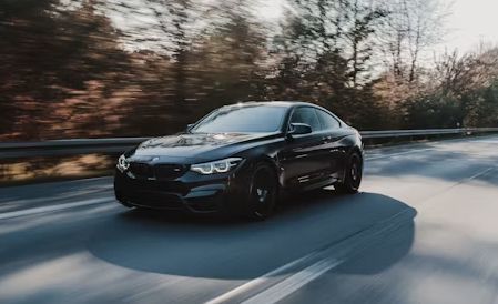 Black sedan driving on a blurred road, surrounded by trees at dusk.