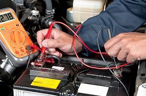 A man is working on a car battery with a multimeter.