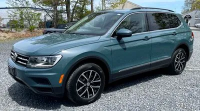 Teal Volkswagen Tiguan SUV parked on gravel, sunny day.
