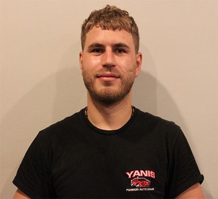 Man standing against a beige wall, wearing a black T-shirt with a small red logo.