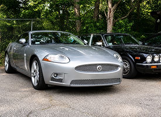 Two silver sports cars parked side by side on a tree-lined street
