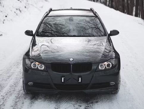 Black BMW station wagon driving on a snowy road.