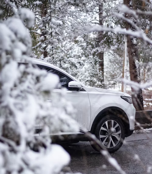 A white car is parked on the side of the road in the snow.