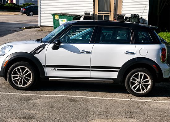 White Mini Cooper parked in a lot beside a building, side view.
