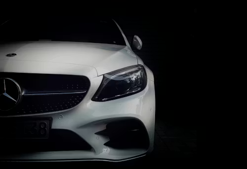 Front view of a white Mercedes-Benz sedan positioned against a pitch-black background.
