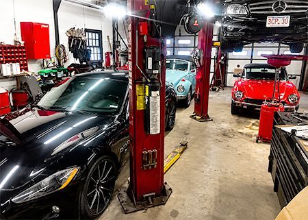 Car repair shop with luxury cars on lifts, including a black sports car in the foreground and red cars in back