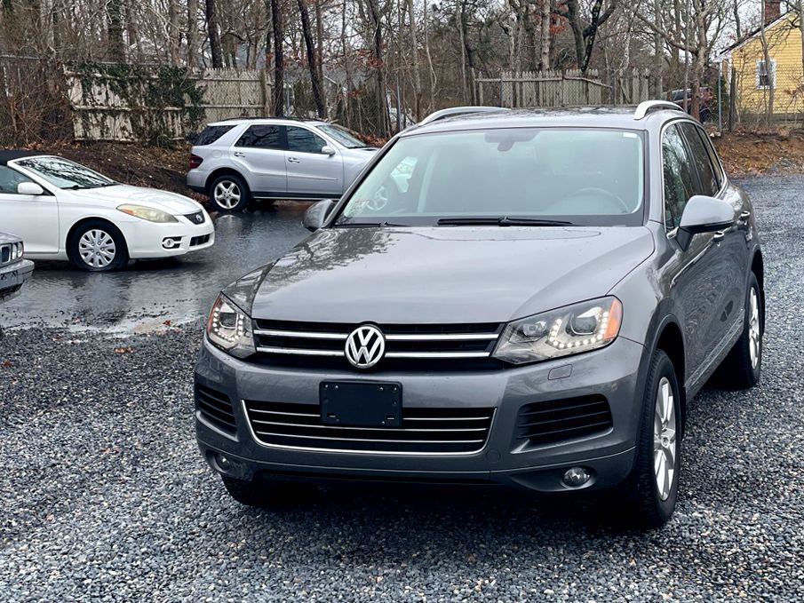 Gray Volkswagen SUV parked on a wet gravel lot with other cars and bare trees behind it
