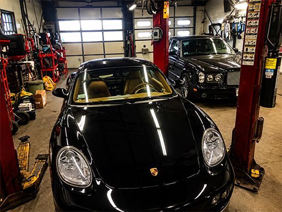a black porsche is parked in a garage next to a rolls royce .