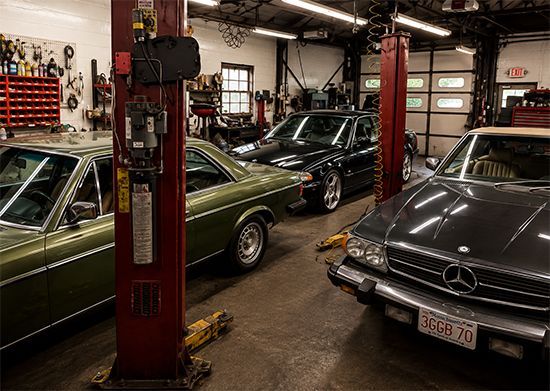 Classic cars parked inside an auto repair garage with a red lift in the foreground