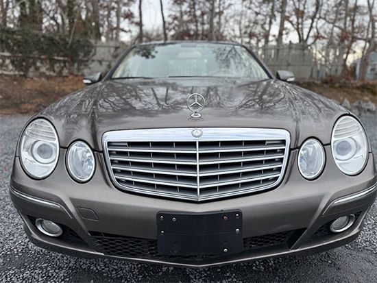 Front view of a silver Mercedes sedan parked outdoors on a wet, wooded roadside