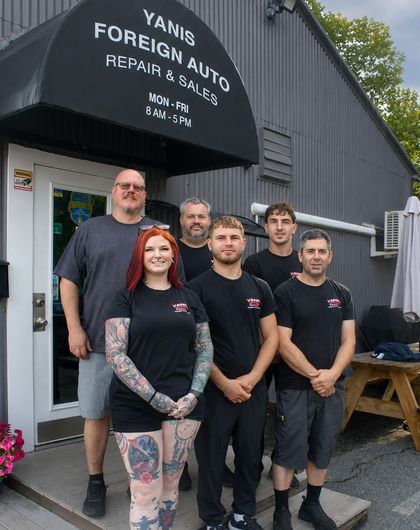 Five mechanics standing outside Yannis Foreign Auto repair shop under the storefront sign
