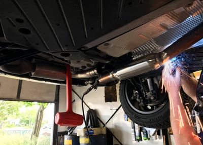 A person is welding under a car in a garage.