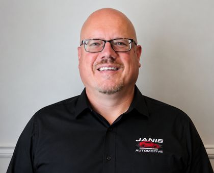 A bald man wearing glasses and a vanis shirt smiles for the camera